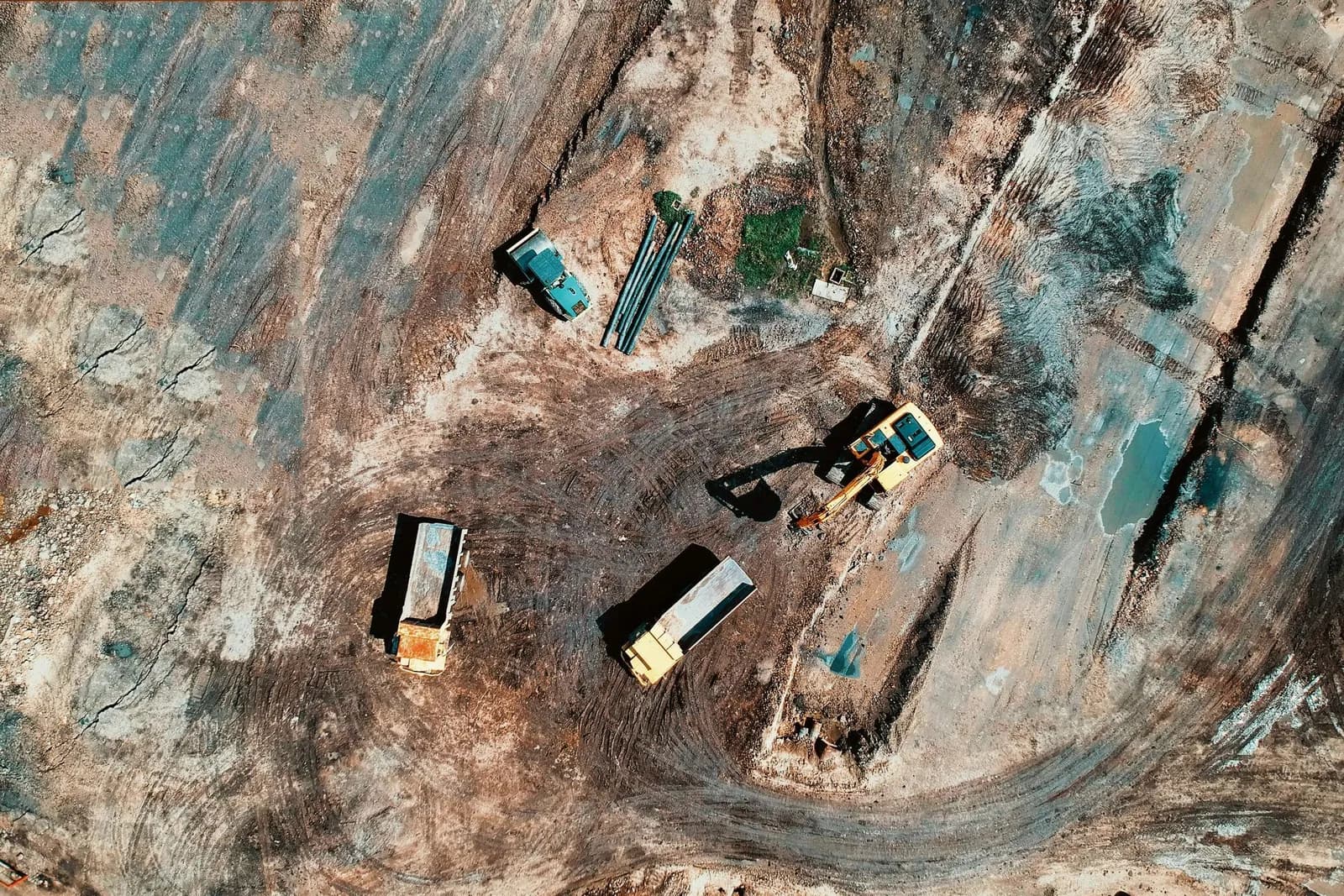 Aerial view of an excavator and dump trucks on a dirt construction site
