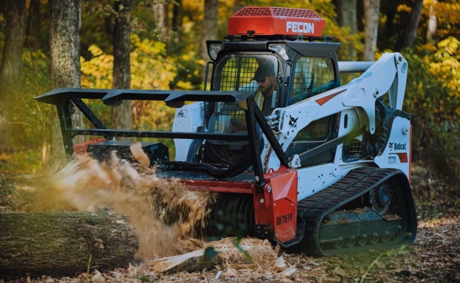 Track loader with a Fecon forestry mulching head grinding a fallen log, wood chips flying
